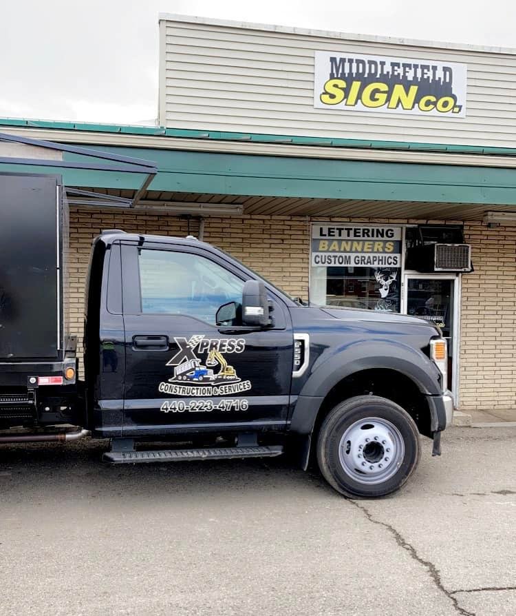 Xpress Construction & Services truck is by a business offering signs, graphics, and yard care services.