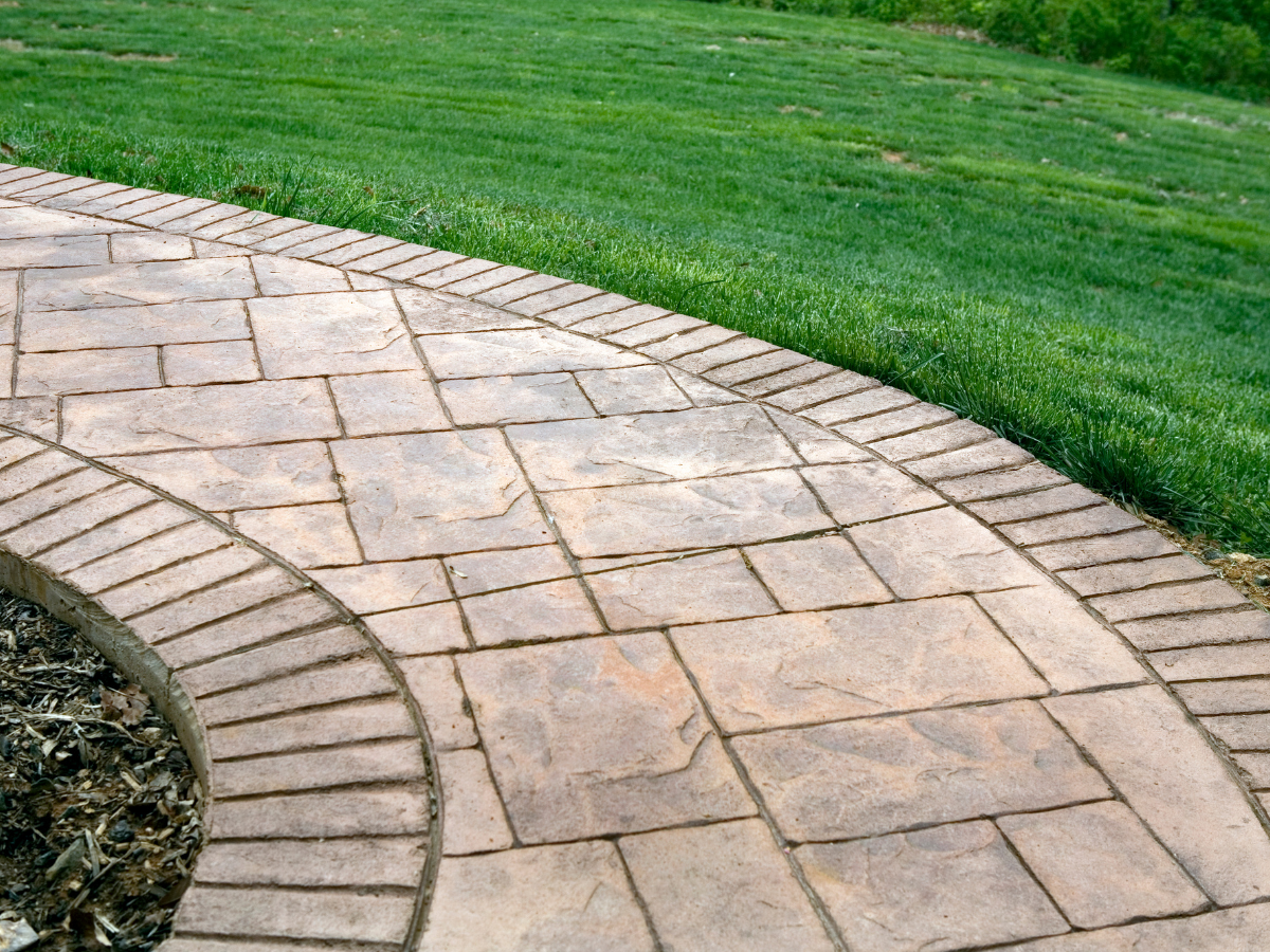 A neat walkway by Xpress Construction & Services showing tidy landscaping, green grass, and expert stonework.